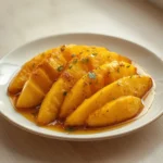 air fryer mango dessert: Glossy caramelized air fryer mango wedges on a white plate with a scoop of melting vanilla ice cream.