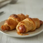 air fryer crescent roll dogs: Golden, flaky air fryer crescent roll dogs with crispy edges on a plate.