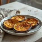 air fryer eggplant: Golden crispy air fryer eggplant slices with charred edges on a plate.