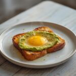 Air Fryer Avocado Toast Eggs: Crispy golden avocado toast with a runny egg yolk in the center, topped on toasted bread in an air fryer.
